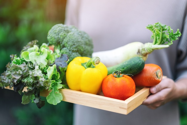 Una donna con in mano un misto di verdure fresche in un vassoio di legno