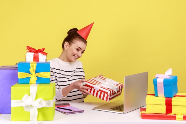Woman holding gift box and looking at laptop screen giving present while having online communication