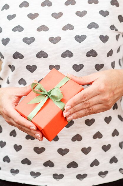 Woman holding a gift box tied with a green ribbon in her hands. Shallow depth of field, Selective focus on the box. Concept of giving a gift on holiday or birthday.