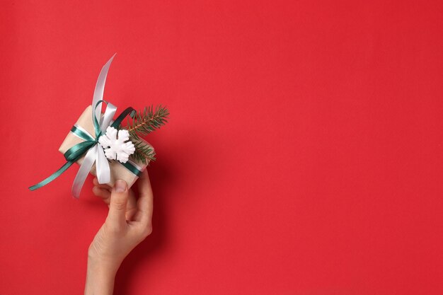 Woman holding giftbox of kraft paper with ribbons on red background. Greeting Xmas card. Boxing day. View from above