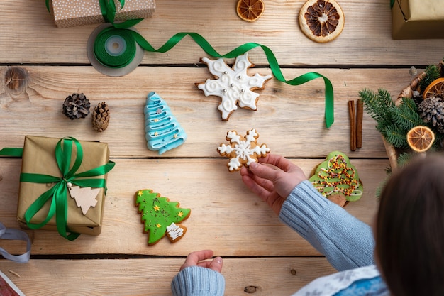 woman holding a gingerbread cookie over a wooden table with ornaments