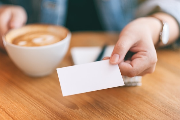 A woman holding and giving a blank empty business card to someone while drinking coffee