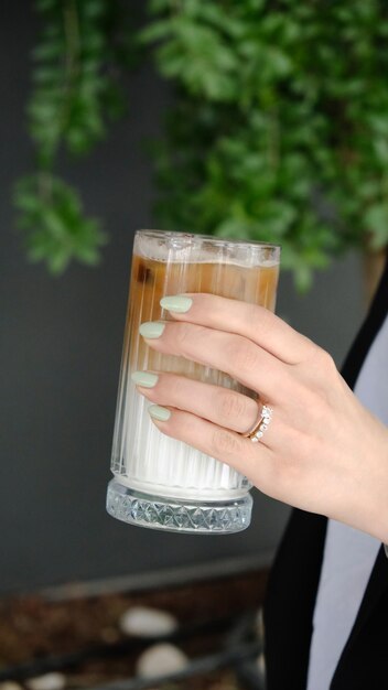 Photo a woman holding a glass of ice water with a green plant in the background