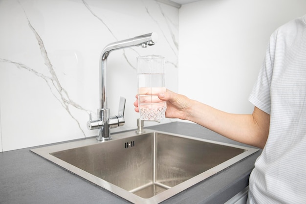 Woman holding a glass pours water from a faucet in the kitchen