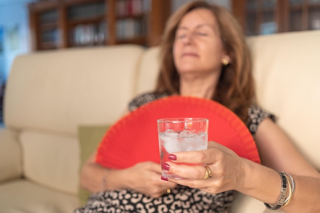 Woman holding a glass of water with ice and a fan to give herself fresh air in a high temperature environment