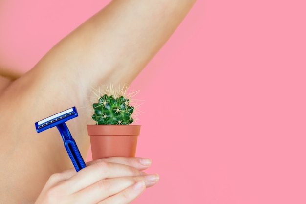 A woman holding a green cactus in a brown pot and a razor near the armpits. the concept of depilation, hair removal and removal unwanted hair on the body.