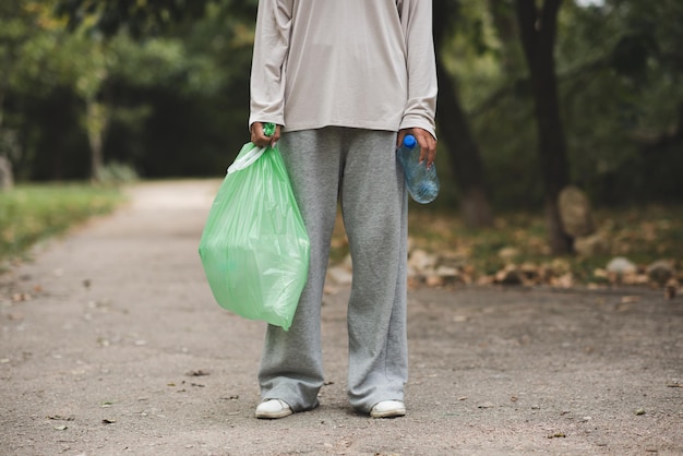 Woman holding green plastic bag with trash and tablet with recycle bottle outdoor Girl help cleaning the environment