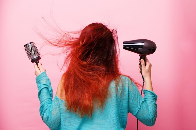 ピンクの背景にヘアドライヤーを保持している女性