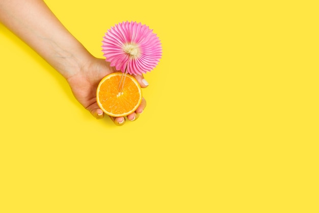 Woman holding a half orange with a pink umbrella on a a yellow background with copy space