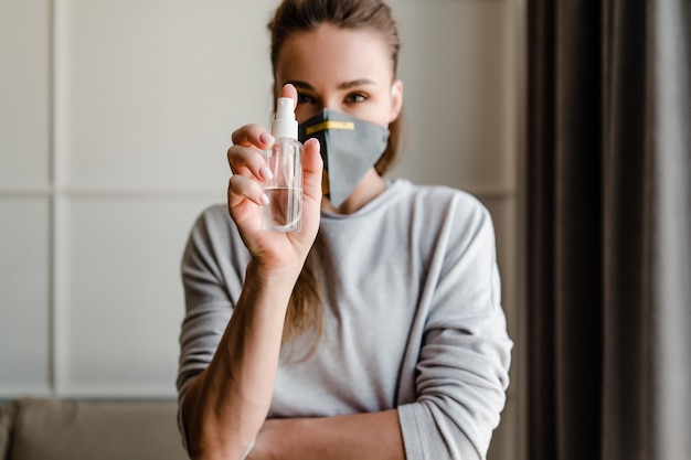 Woman holding hand sanitizer wearing protective mask at home