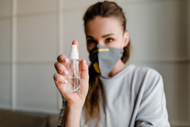 Foto prodotto disinfettante della mano della tenuta della donna che indossa maschera protettiva a casa