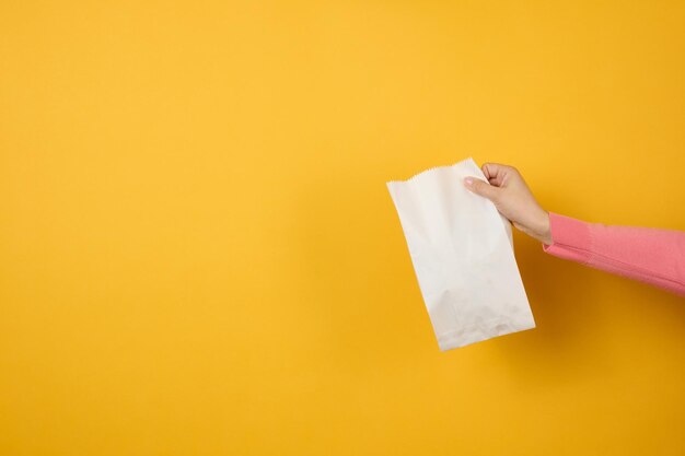 Woman holding in hand white blank craft paper bag for takeaway on yellow background packaging template mock up delivery service concept banner