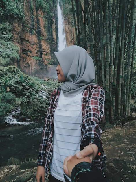 Photo woman holding hands of man standing against waterfall in forest