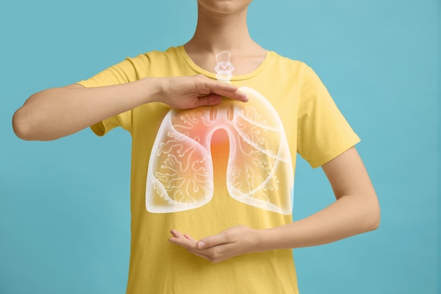 Woman holding hands near chest with illustration of lungs on turquoise background closeup