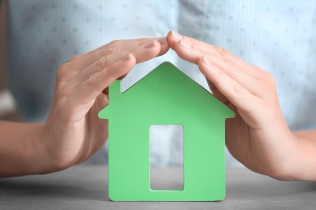 Woman holding hands over wooden figure of house at table close up