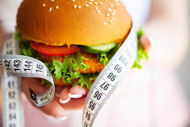 Woman holding harmful fat burger with white measuring tape