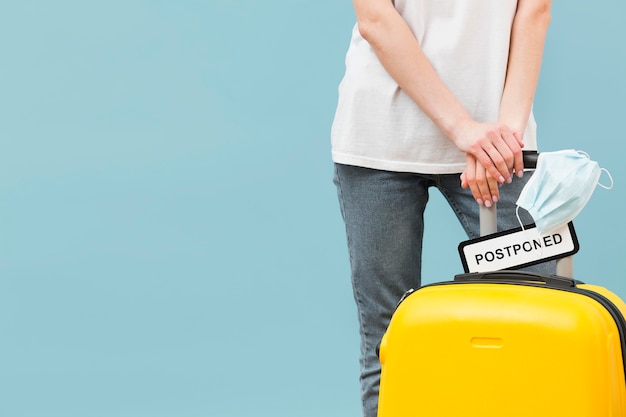 Photo woman holding her baggage with a postponed sign with copy space