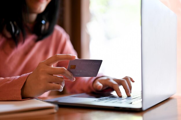 Woman holding her credit card and typing on laptop keyboard cropped shot