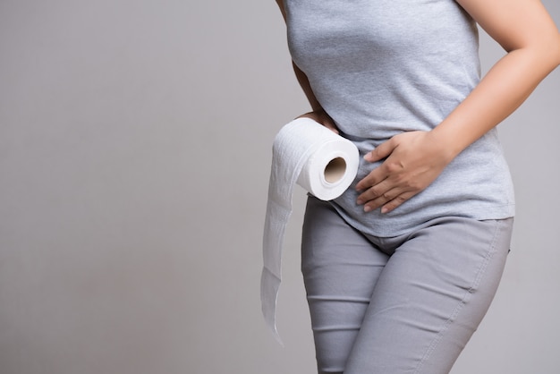 Woman holding her crotch lower abdomen and tissue or toilet paper roll.