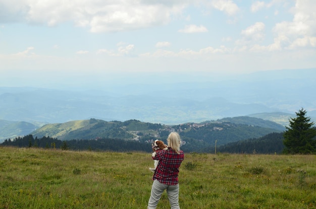 Photo woman holding her dog and watching picturesque mountain landscape