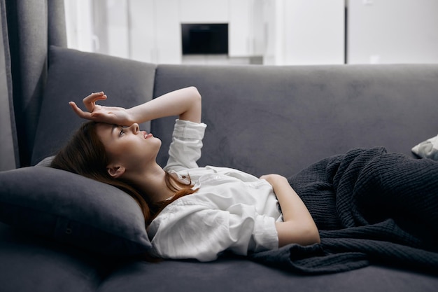 Woman holding her hand on her head lying on the couch feeling unwell