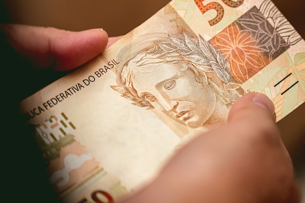 a woman holding in her hands a 50 bill of brazilian money which is the Brazilian Real