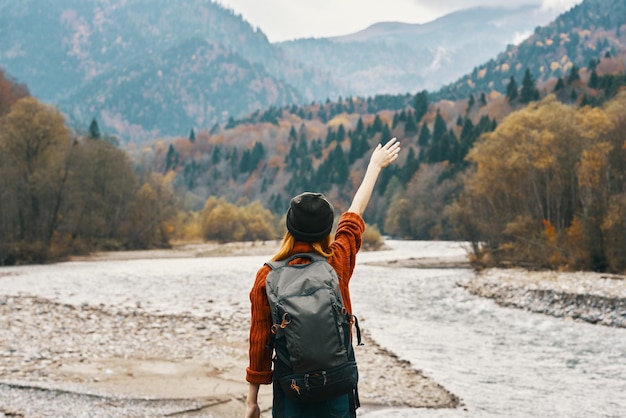 Woman holding her hands above her head in the mountains outdoors in autumn near the river travel