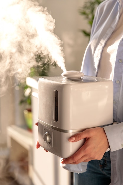 Woman holding in her hands working aroma oil humidifier in sunny room. Humidification of air in the apartment