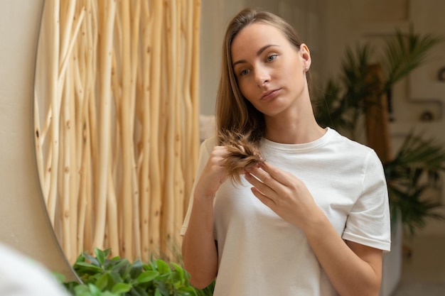 Donna che tiene i suoi capelli lunghi guardando i problemi con le doppie punte danneggiate con la cura dei capelli