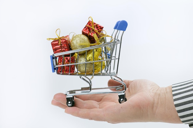 Woman holding on her palm full of Christmas gifts and Christmas decorations little shopping cart