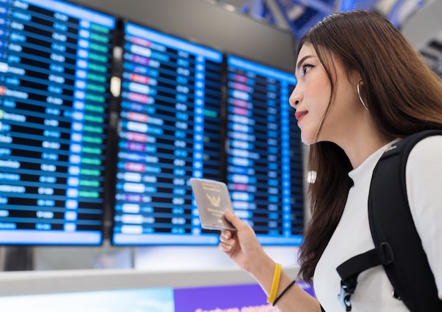 Woman holding her passport with flight information board in international airport 