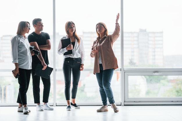 Woman holding her professional camera Group of business people in formal clothes standing indoors near big window