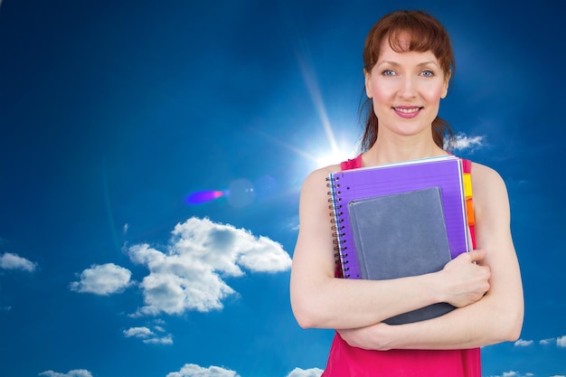Женщина держит свои школьные тетради на фоне облачного неба с солнечным светом