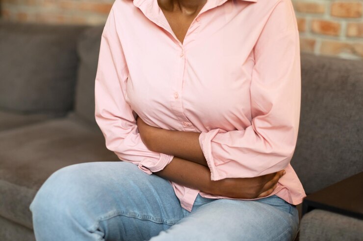 Photo woman holding her stomach in pain while sitting on couch