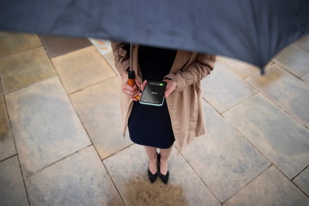 Foto donna che tiene il suo ombrello e chiama qualcuno mentre è fuori quando piove