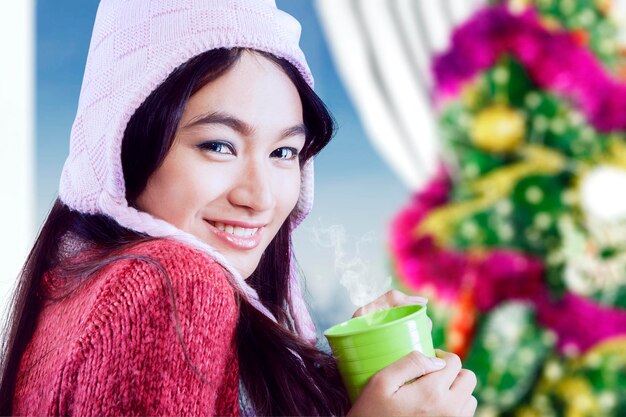 Woman holding hot drink near the Christmas tree