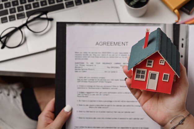 Photo woman holding house model and agreement contract in hand real estate investment and insurance concept