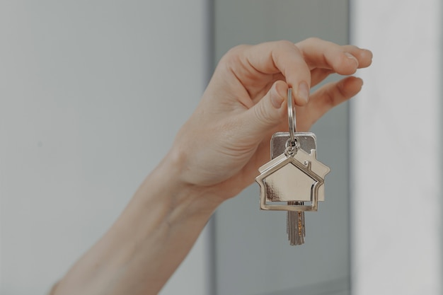 Woman holding house shaped keychain selective focuse on female hand with key from new home