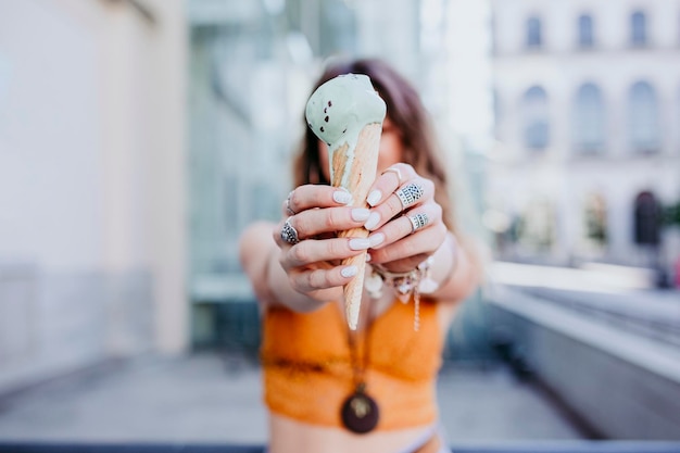 Woman holding ice cream against face while standing against building in city