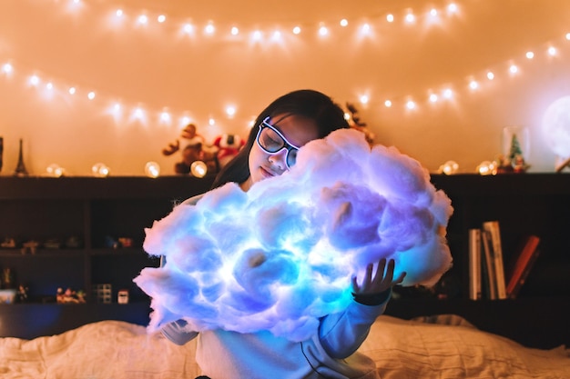woman holding illuminated cloud while sitting on bed at home