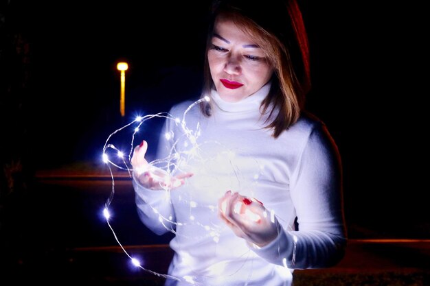 Photo woman holding illuminated string lights in darkroom