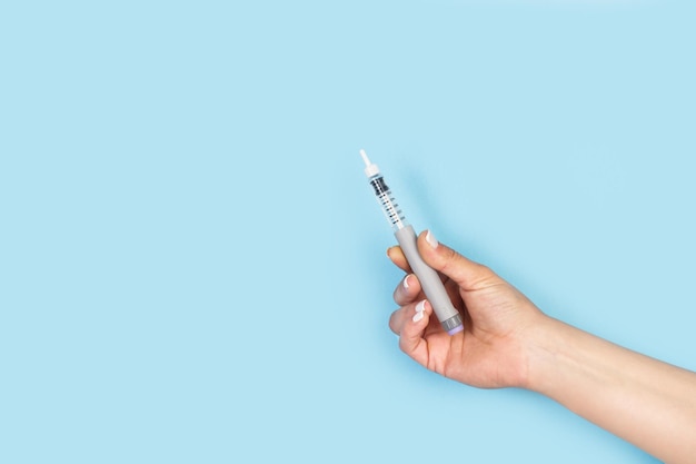 복사 공간이 있는 밝은 파란색 배경에 인슐린 주사 펜을 들고 있는 여성