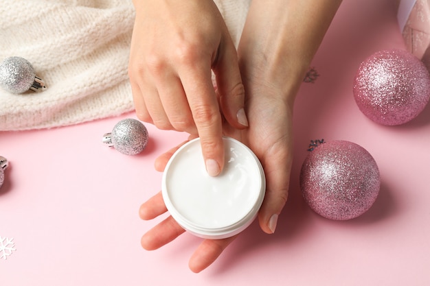 Woman holding jar of cream, warm sweater on pink, space for text. Closeup