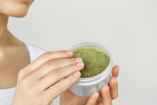 woman holding a jar of salt anticellulite scrub on a gray background