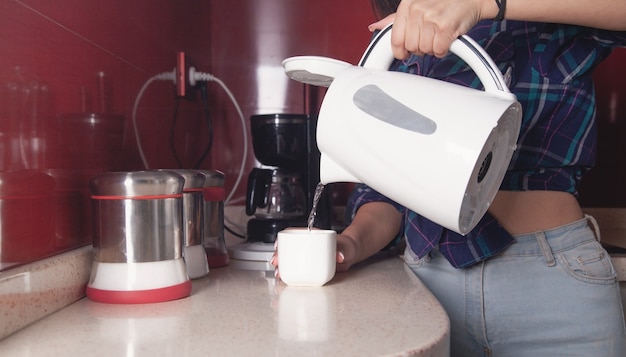 Woman holding kettle and pouring water into cup. Preparing hot drink