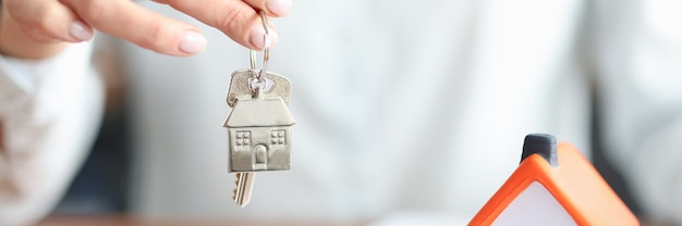 Woman holding key in her hands near toy house closeup