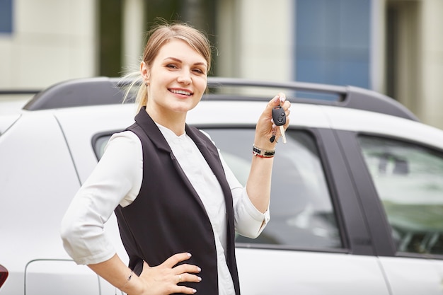 新しい車の自動車のキーを押しながら笑顔の女性