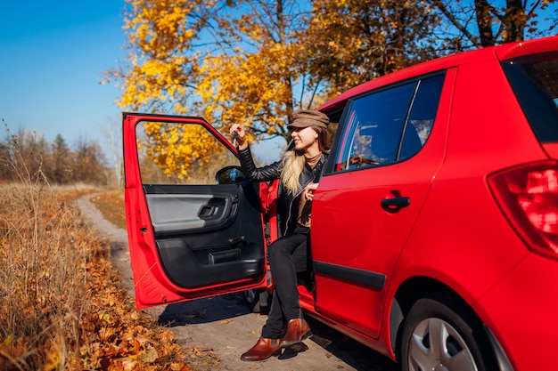 Woman holding keys of new car. happy buyer purchased red autimobile. driver sitting in auto