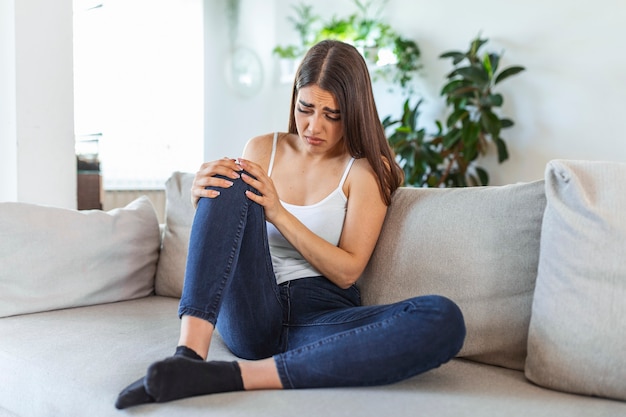 Woman holding the knee with pain on sofa,health care and medical concept.