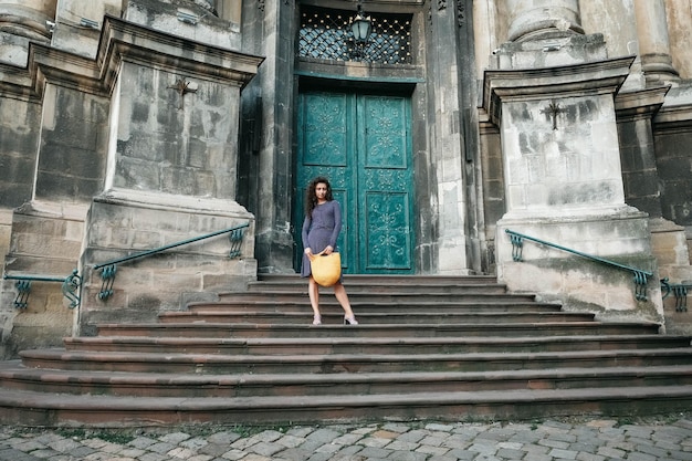 Woman holding knitted yellow bag standing on stairs posing in street of city